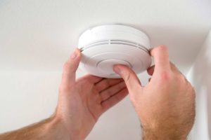 Person fitting fire alarm to ceiling