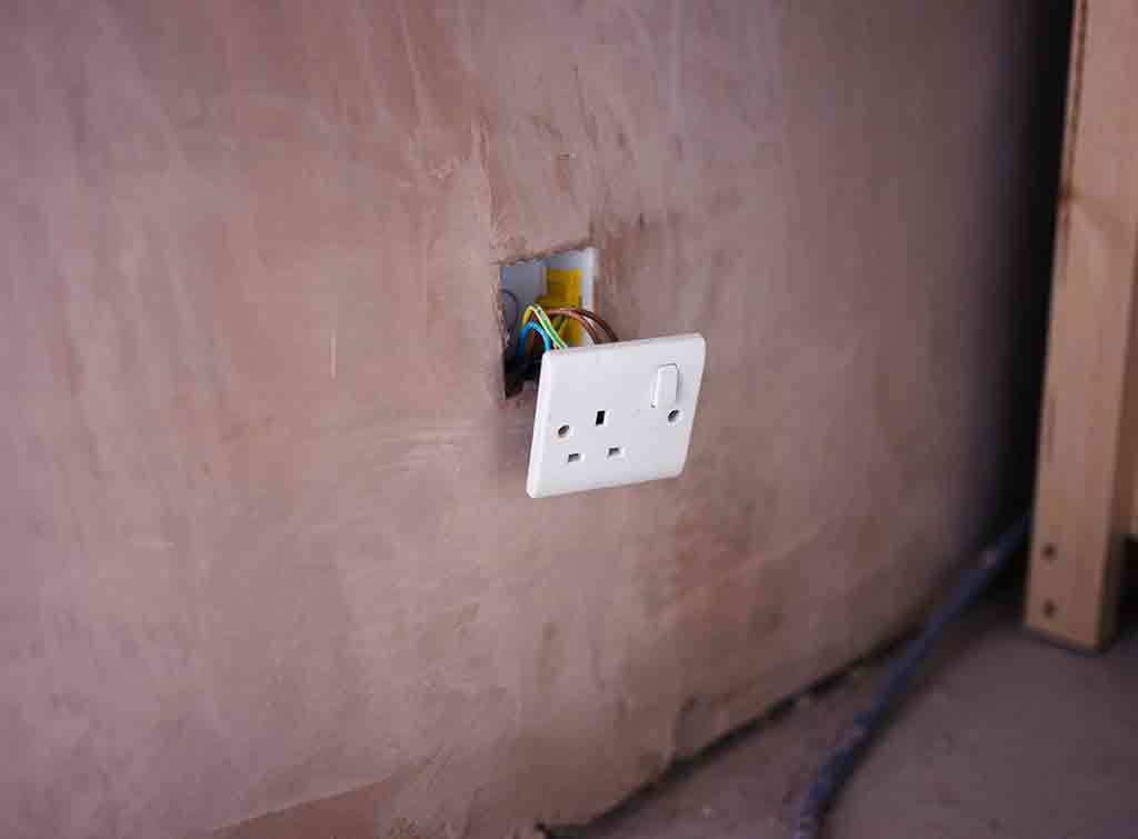 New plug socket being installed in freshly plastered wall