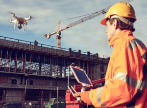 A surveyor in PPE flying a drone over a construction site