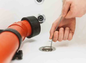How to unblock a bath drain. Person feeding a drain snake down plug hole.