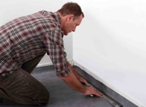 How to cut a skirting board. Image: A man measuring and fitting a skirting board to a plain white wall.