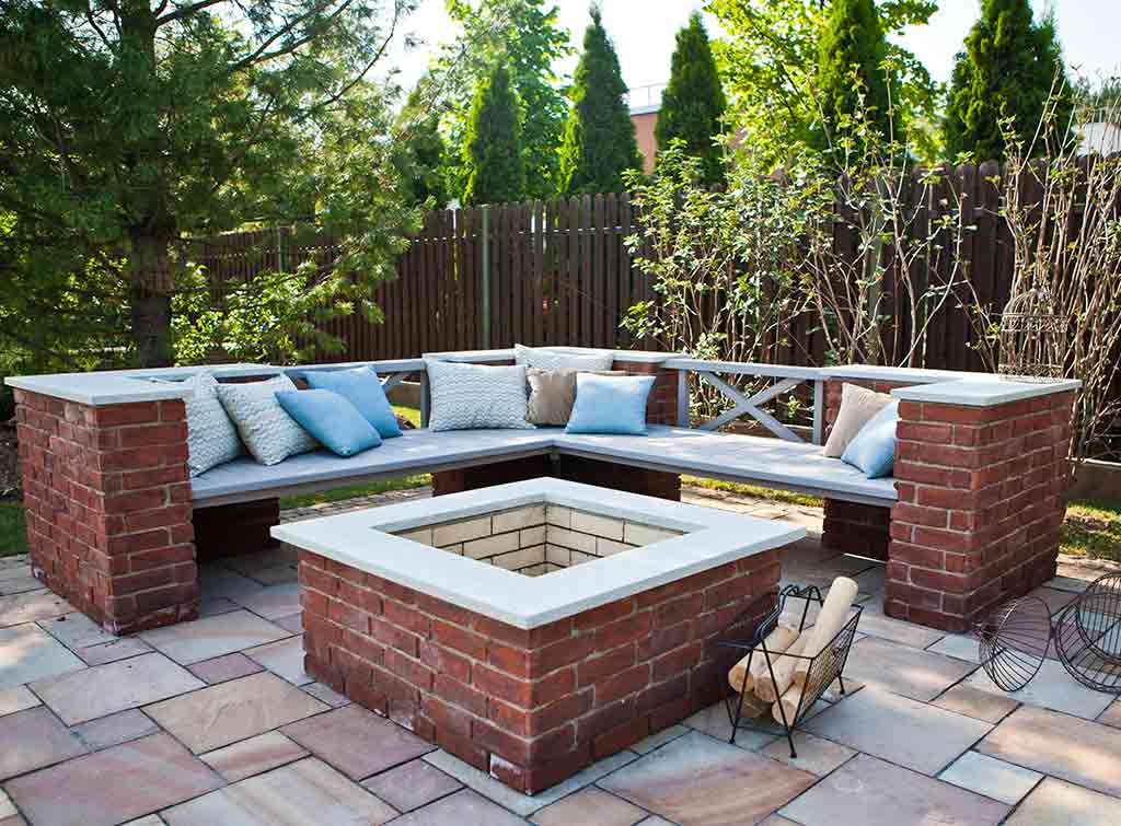 an outdoor fireplace made of bricks, with a bench around it - cheap outoor fireplace ideas