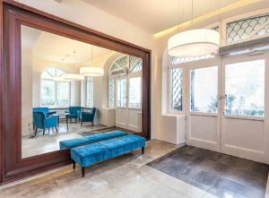A roomwith a large mirror along one wall, with a blue velvet bench in front of it - inexpensive mirror feature wall ideas