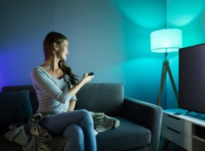 Woman controlling the living room light with a remote - smart lighting installation cost