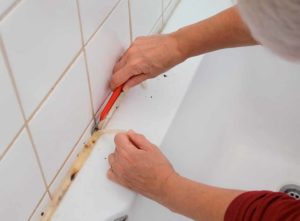 How to reseal a bath. Image: Woman cutting away old bath sealant