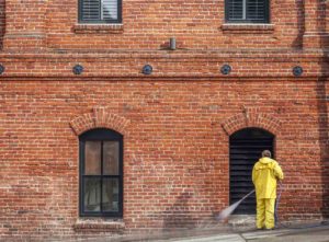 Brick cleaning near me - man in yellow suit spraying the red brick wall