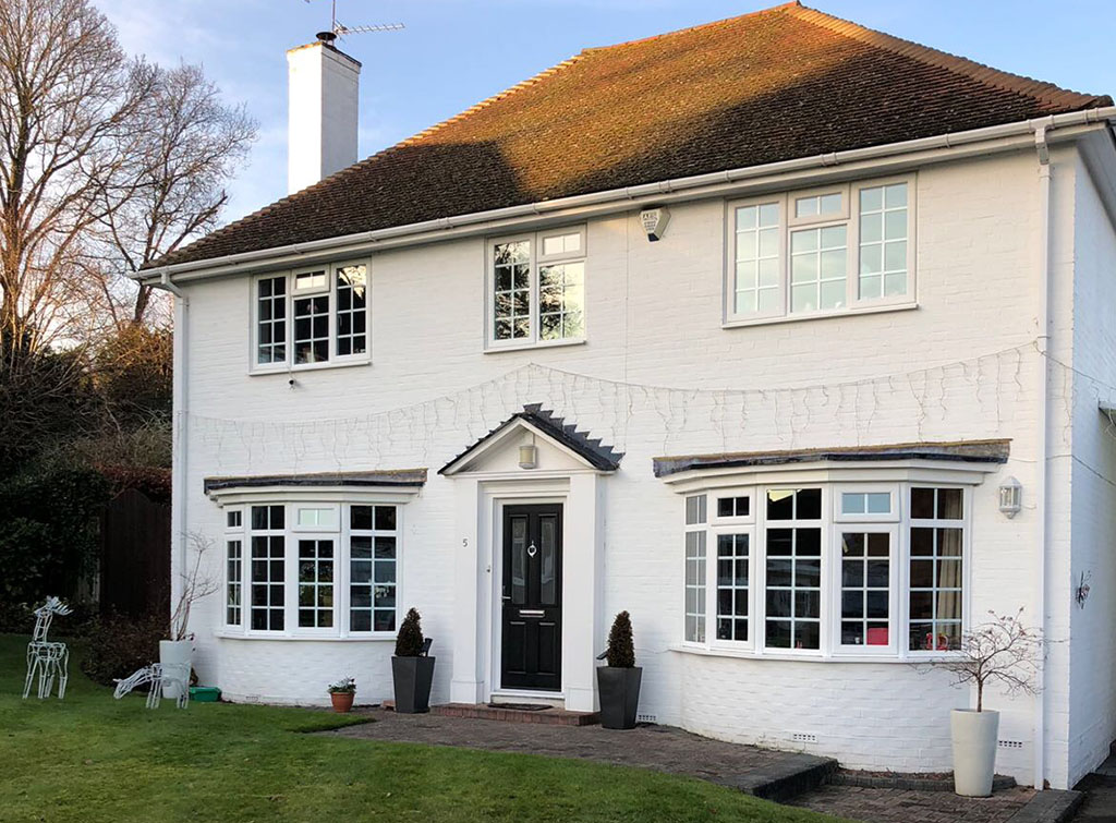 UpVC awning and casement bay windows in a countryside home with a white facade and topiary trees