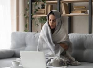 Woman sat with blanket wrapped around her because of cold draughts at home